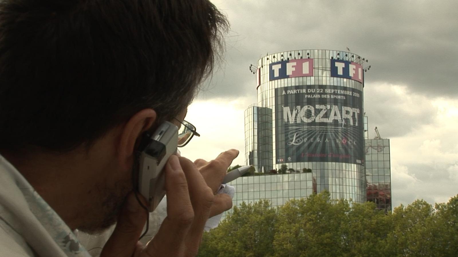 Pierre Carles téléphonant davant le building de TF1 à Paris