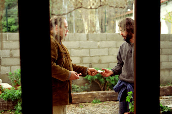 //www.occitanie-films.netDans la cour d'une maison, un homme tend quelque chose à un autre homme, on les voit à travers le cadre de la porte de la maison
