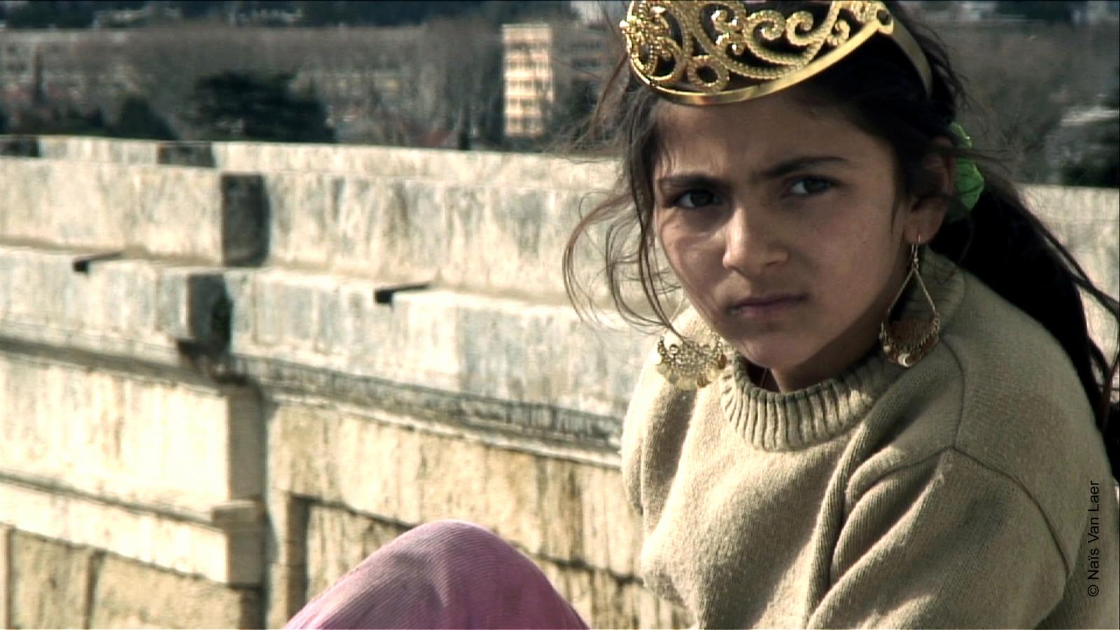 Jeune rom coiffée d'une couronne, adossée contre un mur de pierre